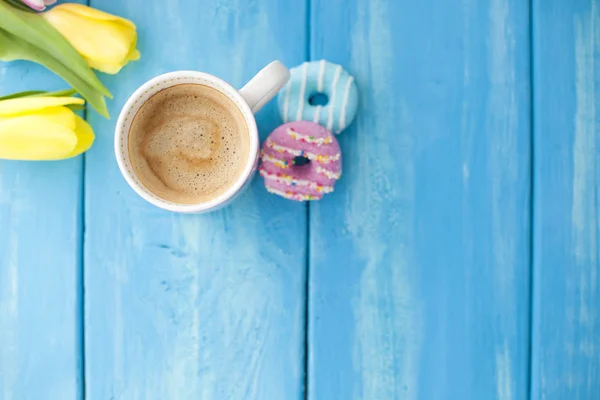 Spring morning, fragrant coffee and tulips of yellow and pink color. Donuttsy copies. Blue wooden background, place for text and postcard