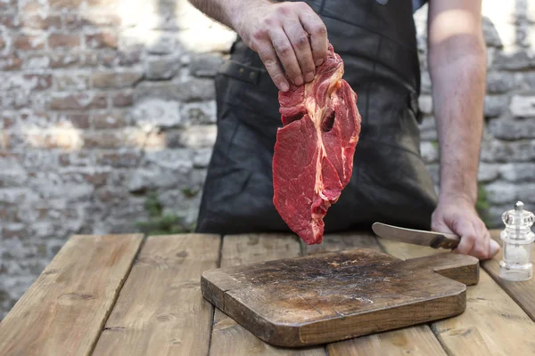Un uomo sta tagliando la carne per cena. Manzo nelle mani di un uomo. Carne rossa e una vecchia tavola di legno. Copia spazio — Foto Stock