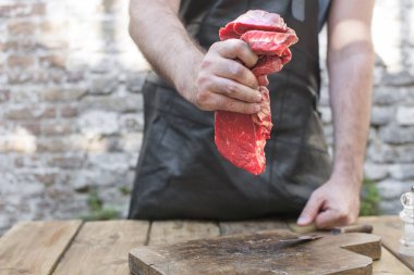 Akşam yemeği için kesim et adamdır. Bir adam elinde sığır eti. Kırmızı et ve eski bir ahşap tahta. Kopya alanı