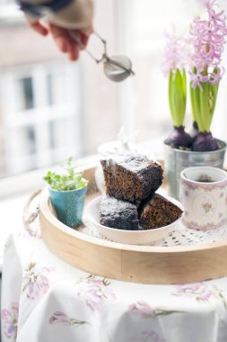 Şeker ve kahve ile çikolatalı kek. Kahvaltı bir ahşap tepsi ve çiçekler. Şehre penceresinden görüntülemek
