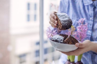 Şeker ve kadınların elinde kahve ile çikolatalı kek. Çiçekler. Pencereden şehre görüntüleyin. Metin veya bir kartpostal için boş alan.