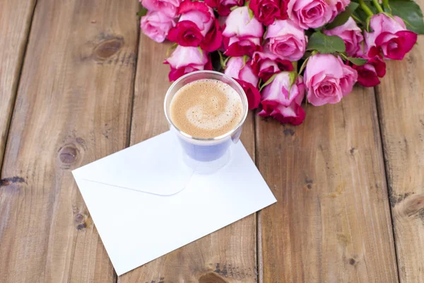 Un bouquet de roses fraîches et un verre d'espresso. Fond en bois. Espace libre pour le texte ou les cartes postales. Enveloppe blanche pour écrire . — Photo