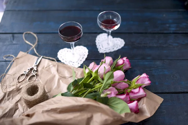 Deux verres de vin rouge sur une table noire, un bouquet de roses en papier brun. Deux cœurs blancs et des biscuits aux macaronis. Espace libre pour texte ou cartes postales . — Photo