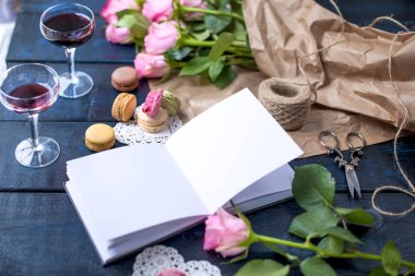 Bir buket gül pembe, gri kağıt ve beyaz bir kalp olduğunu. Açık Not defteri. İki bardak kırmızı şarap. Tatlı makarna macaroons Sevgililer günü farklı renklerde. Metin veya reklam için ücretsiz bir yer