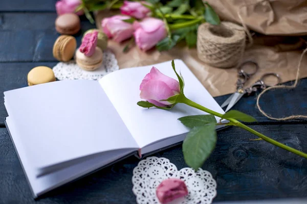 Букет роз розовый, в серой бумаге и белом сердце. Роуз на открытом блокноте. Сладкие макароны разных цветов, в День Святого Валентина. Бесплатное место для текста или рекламы — стоковое фото