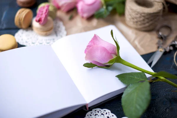 Un ramo de rosas es de color rosa, en papel gris y un corazón blanco. Rose en un cuaderno abierto. Macarrones de pasta dulce de diferentes colores, el día de San Valentín. Un lugar libre para texto o publicidad — Foto de Stock