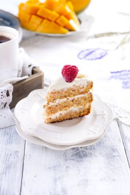 Kahvaltı için bir krem ile küçük bir beyaz tabakta kek kısmı. Mango meyve. Beyaz arka plan, fincan kahve ve boş alan metin veya reklam için