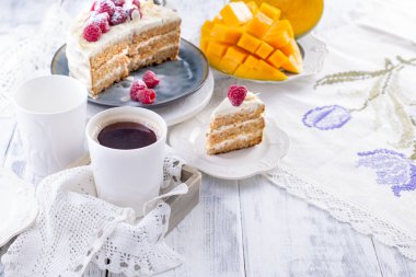 Beyaz kremalı pasta kahvaltı için kesme. Mango meyve. Beyaz arka plan, Masa örtüsü dantel, bir fincan kahve ve metin veya reklam için boş alan ile.
