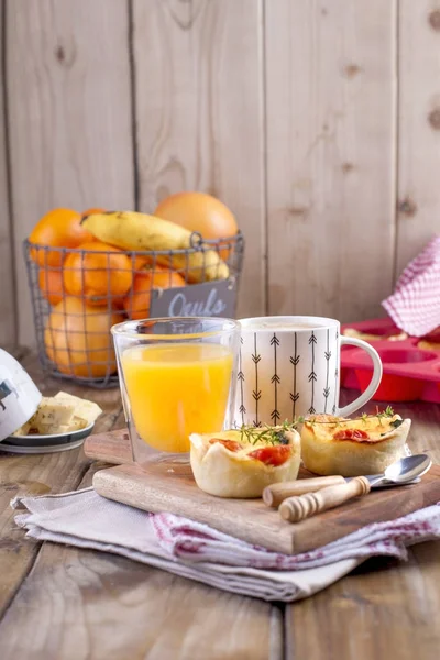 Homemade cupcakes with cheese and cherry tomatoes on a wooden board, spoon and knife. table towel in a red cage, a glass of orange juice and fragrant coffee, with space for writing text or advertising — Stock Photo, Image