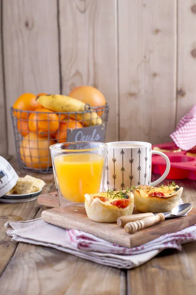 Zelfgemaakte cupcakes met kaas en cherry tomaten op een houten bord, de lepel en het mes. tabel handdoek in een rode kooi, een glas jus d'orange en geurende koffie, met ruimte voor het schrijven van tekst of reclame — Stockfoto