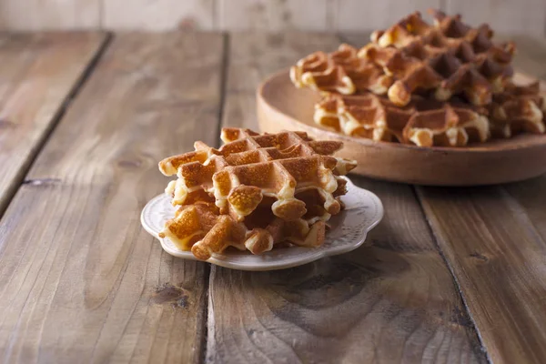Doces waffles belgas para o café da manhã, em um prato de madeira. Em um fundo de madeira marrom . — Fotografia de Stock