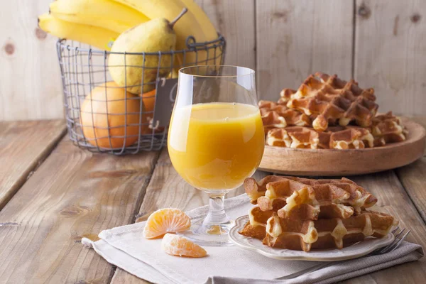 Doces waffles belgas e um copo de suco de laranja para o café da manhã, em um prato de madeira. Cozimento caseiro. Em um fundo de madeira marrom. Espaço livre para texto ou publicidade — Fotografia de Stock