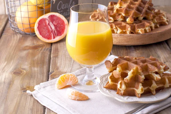 Doces waffles belgas e um copo de suco de laranja para o café da manhã, em um prato de madeira. Cozimento caseiro. Em um fundo de madeira marrom. Espaço livre para texto ou publicidade — Fotografia de Stock