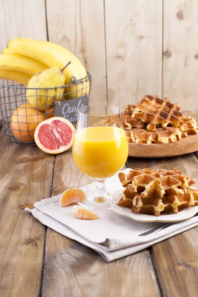Gaufres belges sucrées et un verre de jus d'orange pour le petit déjeuner, sur une assiette en bois. Cuisson maison. Sur un fond brun en bois. Espace libre pour le texte ou la publicité . — Photo