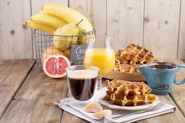 Doces waffles belgas para o café da manhã, decorados com creme branco e molho de chocolate. Copo com café preto e suco de laranja, bananas de frutas e grapfruit em um fundo de madeira marrom. espaço livre para — Fotografia de Stock