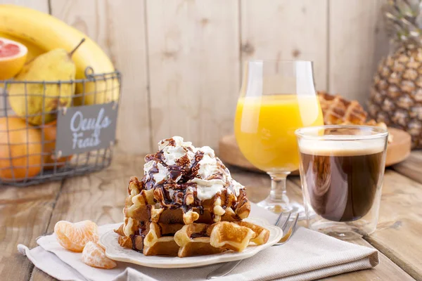 Sweet Belgian waffles for breakfast, decorated with white cream and chocolate sauce. Glass with coffee black and orange juice, fruit bananas and grapfruit on a brown wooden background. free space for — Stock Photo, Image