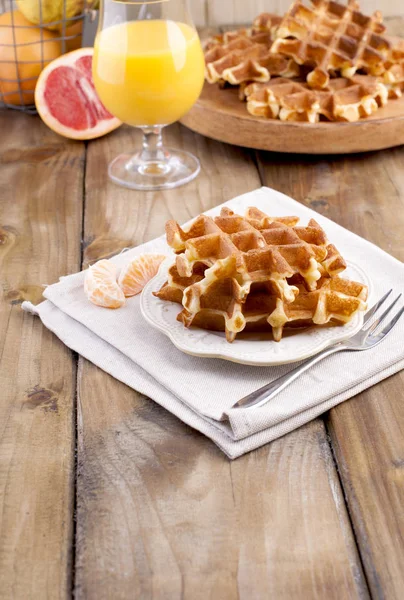 Sweet Belgian waffles and a glass of orange juice for breakfast, on a wooden plate. Homemade baking. On a brown wooden background. Free space for text or advertising. — Stock Photo, Image