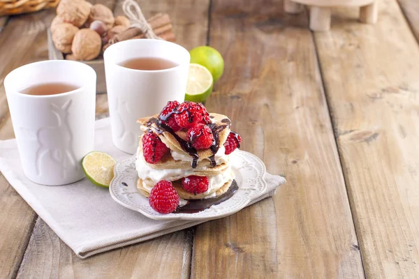 Sweet home punkcakes with white cream and fresh red raspberry berries. Two glasses of tea for breakfast. on a wooden background. free space for text or advertising.