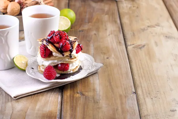 Gâteaux maison sucrés avec crème blanche et framboises rouges fraîches. Deux verres de thé pour le petit déjeuner. sur un fond en bois. espace libre pour le texte ou la publicité — Photo