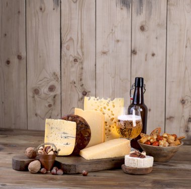 Eski bir ahşap tahta, fındık, aperatifler ve bir bardak bira ve bir şişe farklı peynir klasik seçim.