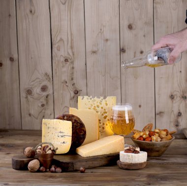 Eski bir ahşap tahta, fındık, aperatifler ve el ile bir şişe farklı peynir klasik seçim, bir bardak bira dökülen.
