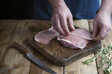Çiğ domuz eti bir ahşap tahta ve bir bıçak, baharatlar ve biberiye, Erkek aşçı eller üzerinde.