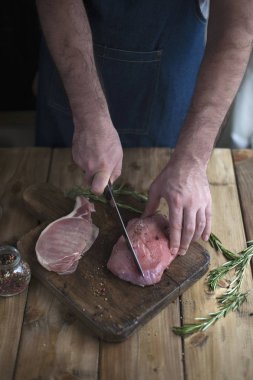 bir adam bir mutfak önlüğü içinde et bir tahta ve bir ahşap masa, biberiye bir bıçakla kesiyor