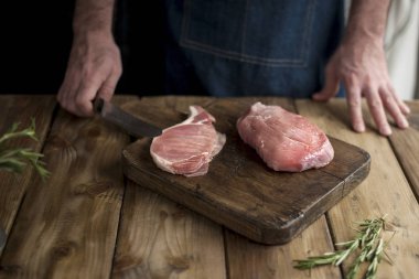 bir erkekte bir mutfak önlüğü, bir yönetim kurulu ve ahşap bir masa, biberiye ve bir bıçak et.