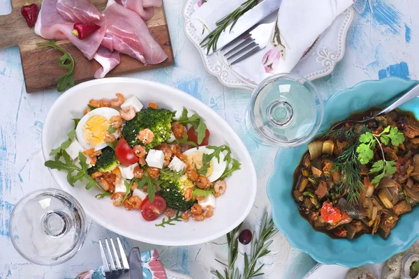 Креветки салат і овочі в білій тарілці і зелені дві склянки вина, а м'ясо на дерев'яній дошці . — стокове фото