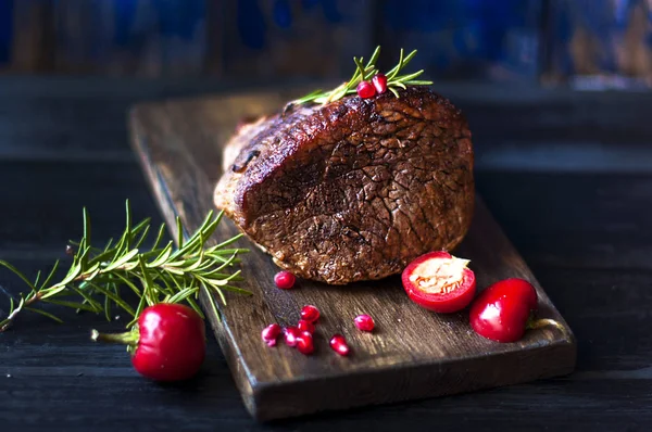 baked meat with rosemary and red pepper. steak. beef. dinner for men. dark photo. Black background. wooden board.