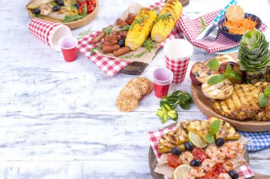 Piknik ızgara gıda ile. Sosis ve Mısır Barbekü, karides, sebze ve meyve. Lezzetli yaz öğle ve plastik yemekleri. Üstten görünüm.