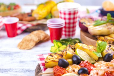 Piknik ızgara gıda ile. Sosis ve Mısır Barbekü, karides, sebze ve meyve. Lezzetli yaz öğle ve plastik yemekleri. Üstten görünüm.