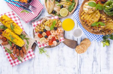 Piknik ızgara gıda ile. Sosis ve Mısır Barbekü, karides, sebze ve meyve. Lezzetli yaz öğle ve plastik yemekleri. Üstten görünüm.
