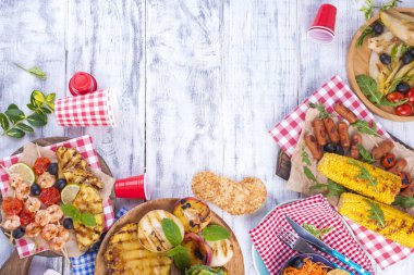 Piknik ızgara gıda ile. Sosis ve Mısır Barbekü, karides, sebze ve meyve. Lezzetli yaz öğle ve plastik yemekleri. Üstten görünüm.