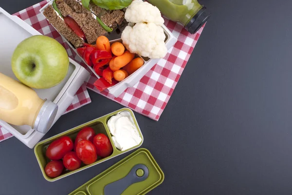 Leckeres Mittagessen in einem Container für Schule und Büro. Sandwich, Gemüse, Apfel und grüner Saft für ein gesundes Mittagessen. Draufsicht auf schwarzem Hintergrund. Kopierraum — Stockfoto