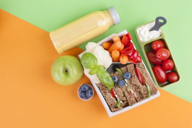 Sandviç ve meyve parlak bir arka plan üzerinde beslenme çantası ile taze meyve suyu. Sağlıklı bir öğle yemeği şallar, ofis ve üniversite için. Kitap ve kitap okul. Üstten görünüm.