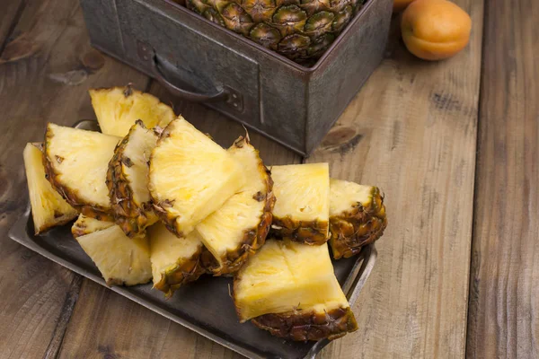 A large and ripe pineapple is cut into pieces, and a whole fruit. Tropical fruit on a wooden background. Free space for text. Copy space — Stock Photo, Image