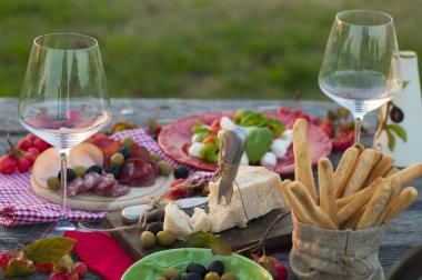 Kırmızı şarap, Parmesan, jambon, caprese salatası ve zeytin ile İtalyan piknik. Açık havada yemek ve ahşap masa ve yeşil çim. Geleneksel aperatifler.