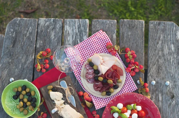 Picnic italiano con vino tinto, parmesano, jamón, ensalada de caprese y aceitunas. Almuerzo al aire libre y mesa de madera. Aperitivos tradicionales. Copiar espacio — Foto de Stock