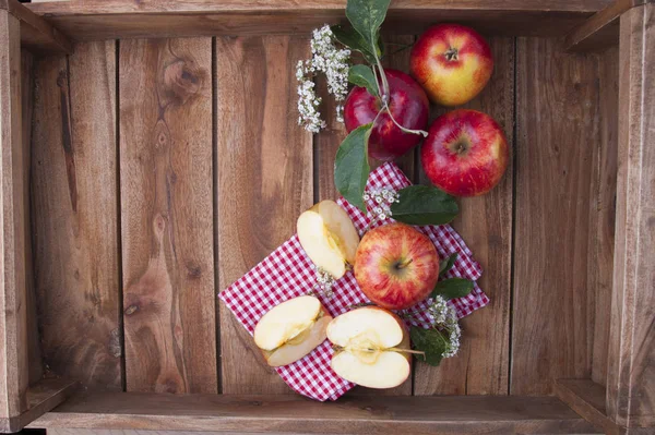 Red apples on a wooden box with leaves and flowers. Autumn harvest of fruits. Top view. Free space for text. — Stock Photo, Image
