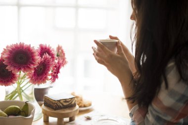 Bir kadın kahvaltı penceresinde, bir buket çiçek ve hoş kokulu kahve masada yiyor. Günaydın evde. Metin için boş alan.