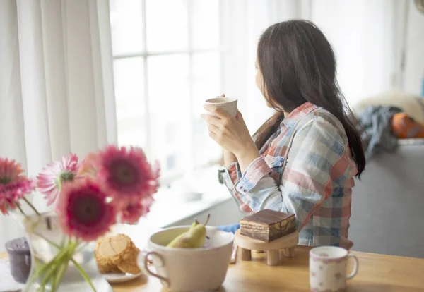 Woman with a mug of coffee, a good morning at home. Breakfast and fragrant coffee. The interior is cozy and the flowers. Free space for text.