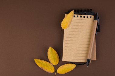 Kahverengi bir arka plan üzerine notlar için açık bir not defteri. Metin için özgür yer. Sonbahar atmosfer ve sarı yapraklar. Üstten görünüm. Düz yatıyordu. Kopya alanı.