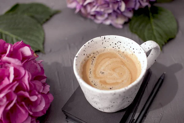Hortênsias roxas frescas em fundo cinza. Uma xícara de café da manhã aromático e um bloco de notas para planejar o dia. Espaço livre para texto. Vista superior. Espaço de cópia . — Fotografia de Stock