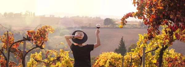 Ragazza con un cappello al tramonto e un bicchiere di vino in mano. Natura Italia, colline e campi di uva alla luce del sole. Riflessi e raggi di sole nella cornice. Spazio libero per il testo. Copia spazio . — Foto Stock