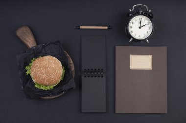 Büyük hamburger susam siyah bir arka plan ile. Fast food ve metin için özgür yer. Not defteri ve Defter kayıtları ve günün planlama. Yukarıdan görüntüleyin. Düz yatıyordu.