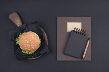 Büyük hamburger susam siyah bir arka plan ile. Fast food ve metin için özgür yer. Defter kayıtları, okul ve ofis için günü planlama. Yukarıdan görüntülemek.