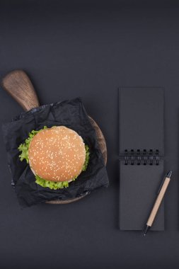 Büyük hamburger susam siyah bir arka plan ile. Fast food ve metin için özgür yer. Defter kayıtları, okul ve ofis için günü planlama. Yukarıdan görüntülemek