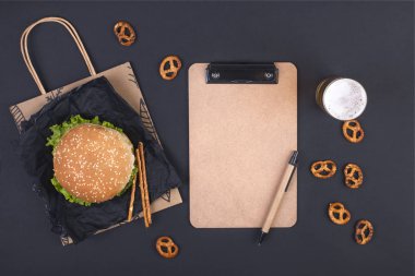 Büyük hamburger, bira ve bir siyah arka plan üzerinde planlama için defter. Fast food ve aperatifler. Metin için özgür yer. Düz yatıyordu. Kopya alanı.