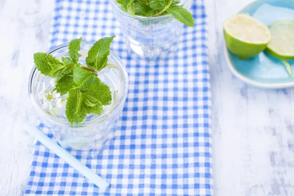 Water with mint and ice in a glass. refreshments in the summer. Full background and two glasses